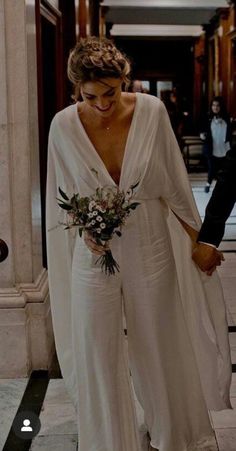 a woman in a white dress walking down a hallway with a bouquet on her hand