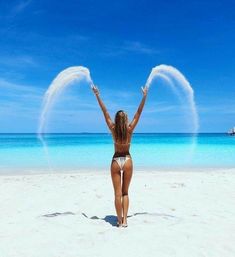 a woman standing on top of a sandy beach next to the ocean with her arms in the air