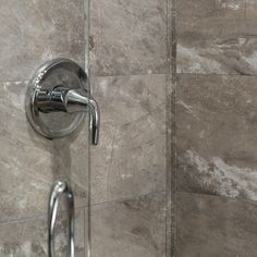 a shower head and hand rail in a tiled bathroom stall with marble tiles on the walls