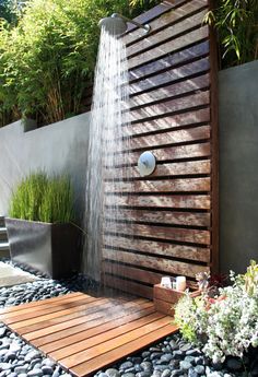 an outdoor shower with wooden slats and water flowing from the faucet, surrounded by rocks