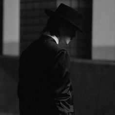 a man in a suit and fedora walking down the street with his hat on