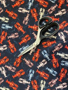 a pair of scissors sitting on top of a blue and red print fabric with lobsters