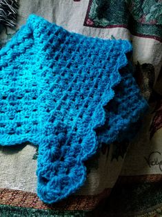 a blue crocheted blanket laying on top of a bed next to a pillow