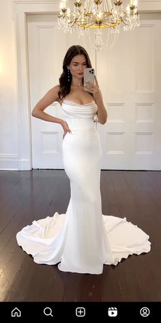 a woman in a white dress taking a selfie with her cell phone while standing on a wooden floor