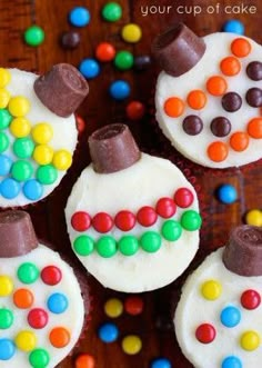 four cupcakes decorated with white frosting and colorful candies on a wooden table