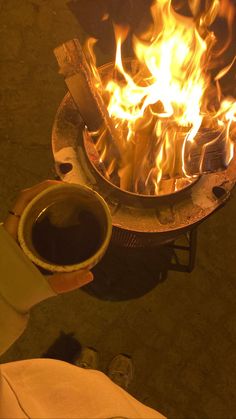 a person holding a coffee cup in front of a fire pit with flames on it