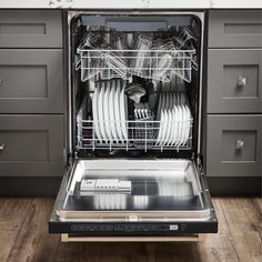 an open dishwasher sitting on top of a wooden floor next to gray cabinets