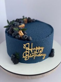 a blue birthday cake with gold lettering and berries on the top that says happy birthday