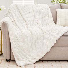 a couch with a white blanket on top of it next to a plant and window