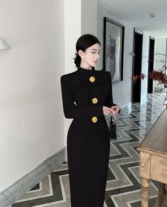 a woman in a black dress standing next to a table with a purse on it