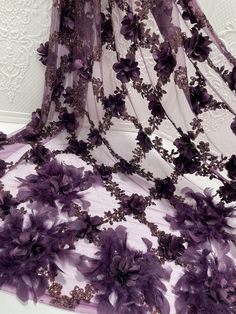 purple flowers and lace are on the sheered fabric that is draped over a white wall