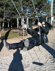 a man in leather clothes swinging on a swing set with his shadow projected on the ground