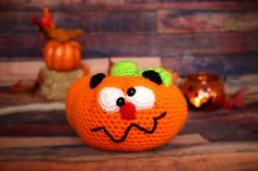 a crocheted orange with a face on it's side sitting next to other pumpkins