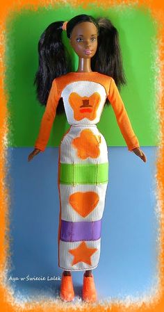 a doll wearing an orange and white dress with fish on it's back, standing in front of a green background