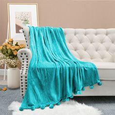 a white couch with a turquoise blanket on top of it next to a flower vase