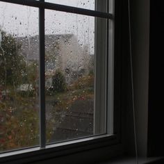 a window with rain drops on it and a house in the back ground behind it