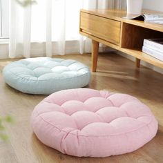 two round cushions sitting on the floor in front of a wooden table with books and a plant