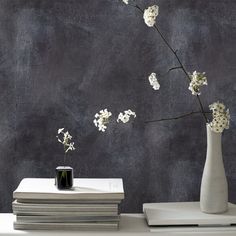 a white vase with flowers on top of a stack of books next to a black wall