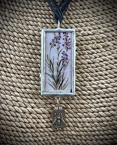 a necklace with an image of lavender flowers hanging from it's side on a woven piece of cloth