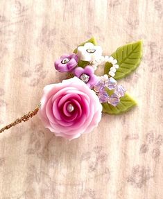 a pink flower with green leaves on a white table cloth and bead trimmings