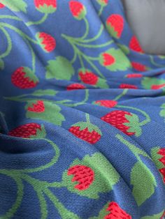 a blue and green blanket with red strawberries on it, next to a gray couch