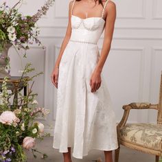 a woman wearing a white dress standing in front of a chair and flowers on the floor