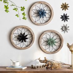 three circular wooden wall hangings with flowers and leaves on them next to a coffee cup