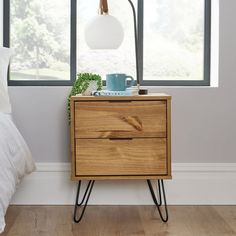 a nightstand with two drawers and a lamp on it in front of a large window