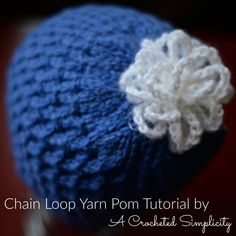 a blue and white crocheted hat with a flower on the side, text chain loop yarn pom - pom by a created simply