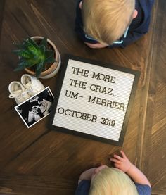 a young boy sitting next to a sign that reads the more the craz um merrier