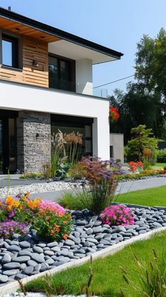 a modern house with flowers and rocks in the front yard, as well as landscaping