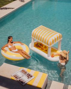 two women sitting on inflatable rafts next to a swimming pool with food