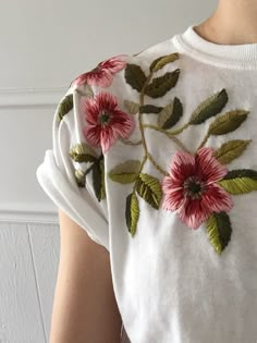 a woman wearing a white t - shirt with pink flowers and green leaves on it