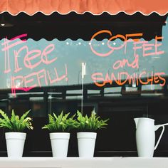 three potted plants sitting in front of a coffee shop's window with the words free coffee and sandwiches written on it