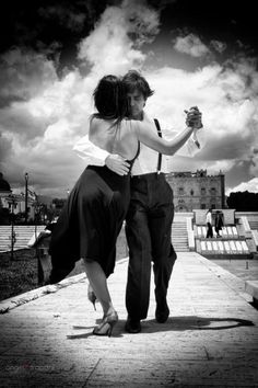 a man and woman dance on the sidewalk in front of some benches under a cloudy sky