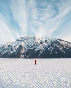 a person standing in the middle of a snow covered field with mountains in the background