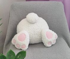 a white teddy bear sitting on top of a gray chair next to a green plant