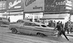 an old photo of people and cars on the street in front of stores with advertisements