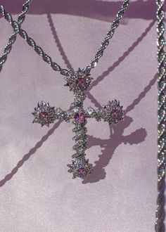 a necklace with a cross hanging from it's side on a purple cloth background