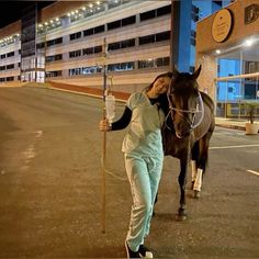 a woman is standing next to a horse and holding a pole in front of a building