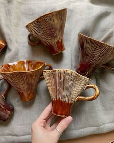 a hand is pointing at four coffee cups on a tablecloth with other items in the background