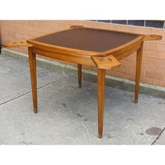 a wooden table sitting on top of a sidewalk next to a brick wall in front of a building