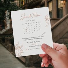 a person holding up a wedding card in front of a building with stairs and trees