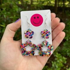 a person holding up a card with some earrings on it and a smiley face in the middle