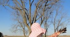 a woman in a pink and white dress flying a kite next to a bare tree