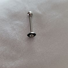 a black and silver nose piercing on a white sheeted surface with the letter g