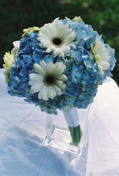 a bouquet of blue and white flowers in a vase on top of a cloth covered table