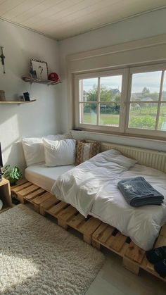 a bed made out of wooden pallets in a room with two windows and a rug on the floor