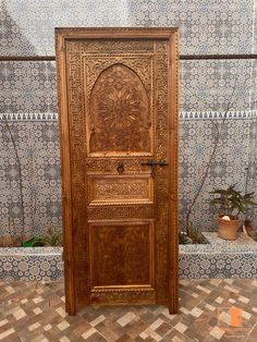 an intricately carved wooden door sits in front of a tiled wall with potted plants