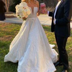 a bride and groom standing in the grass at their outdoor wedding ceremony, drinking champagne